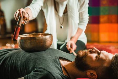 sound healing practitioner playing singing bowl on a person one on one.